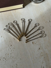 Ten Hermes champagne stirrers fanned out on travertine, figure eight loop tops above twisted silver stems and gilt tips