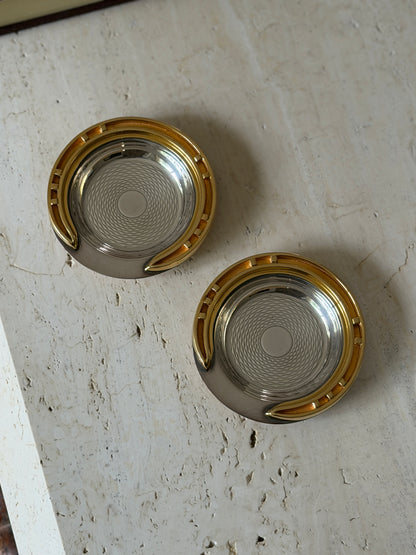Two Hermes guilloche ashtrays with applied brass horseshoe rims shown from above on a travertine table