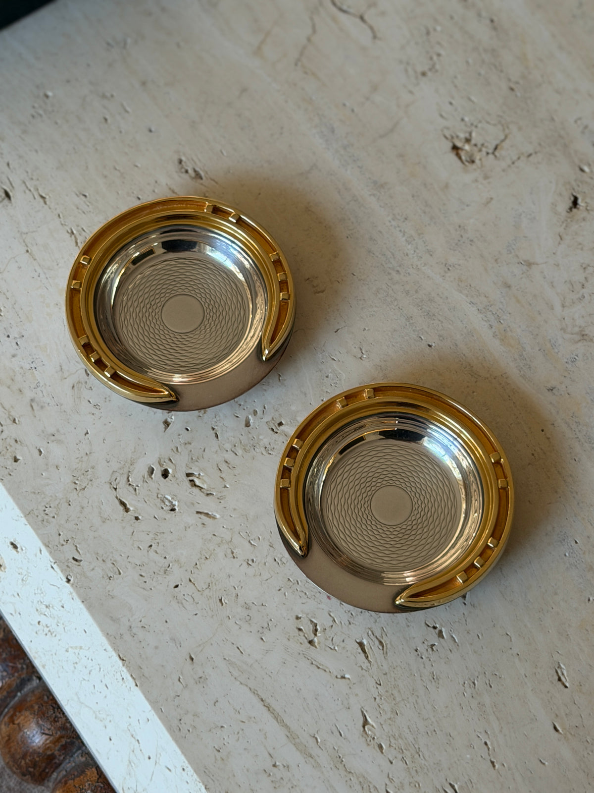 Pair of Hermes horseshoe ashtrays at an angle, showing the gilt horseshoe with raised nail detailing around the silver-tone bowl