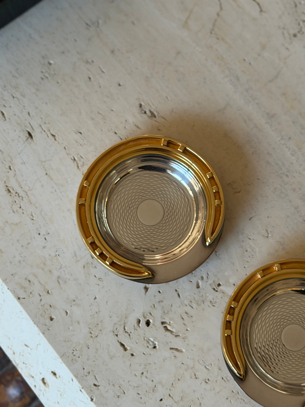 Close view of one Hermes ashtray highlighting the engine-turned guilloche wave pattern in the polished silver-tone center