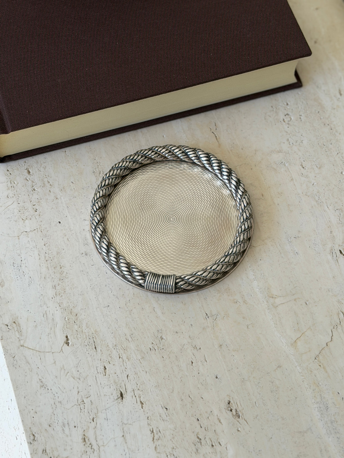 Hermes guilloche bottle coaster with a twisted cordage rope rim and wrapped binding, the center engine turned in concentric waves, on travertine
