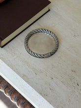 Hermes rope rim coaster on a travertine console near a brown book, the bobbin turned table leg visible below
