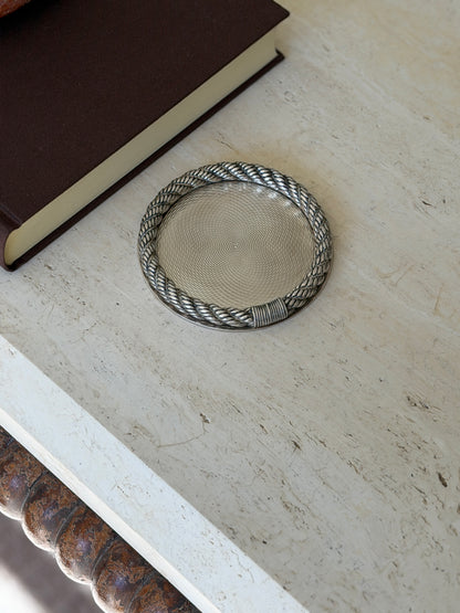 Hermes rope rim coaster on a travertine console near a brown book, the bobbin turned table leg visible below