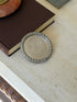 Hermes cordage coaster resting against a brown book, the oxidized rope twist framing the radiating guilloche center