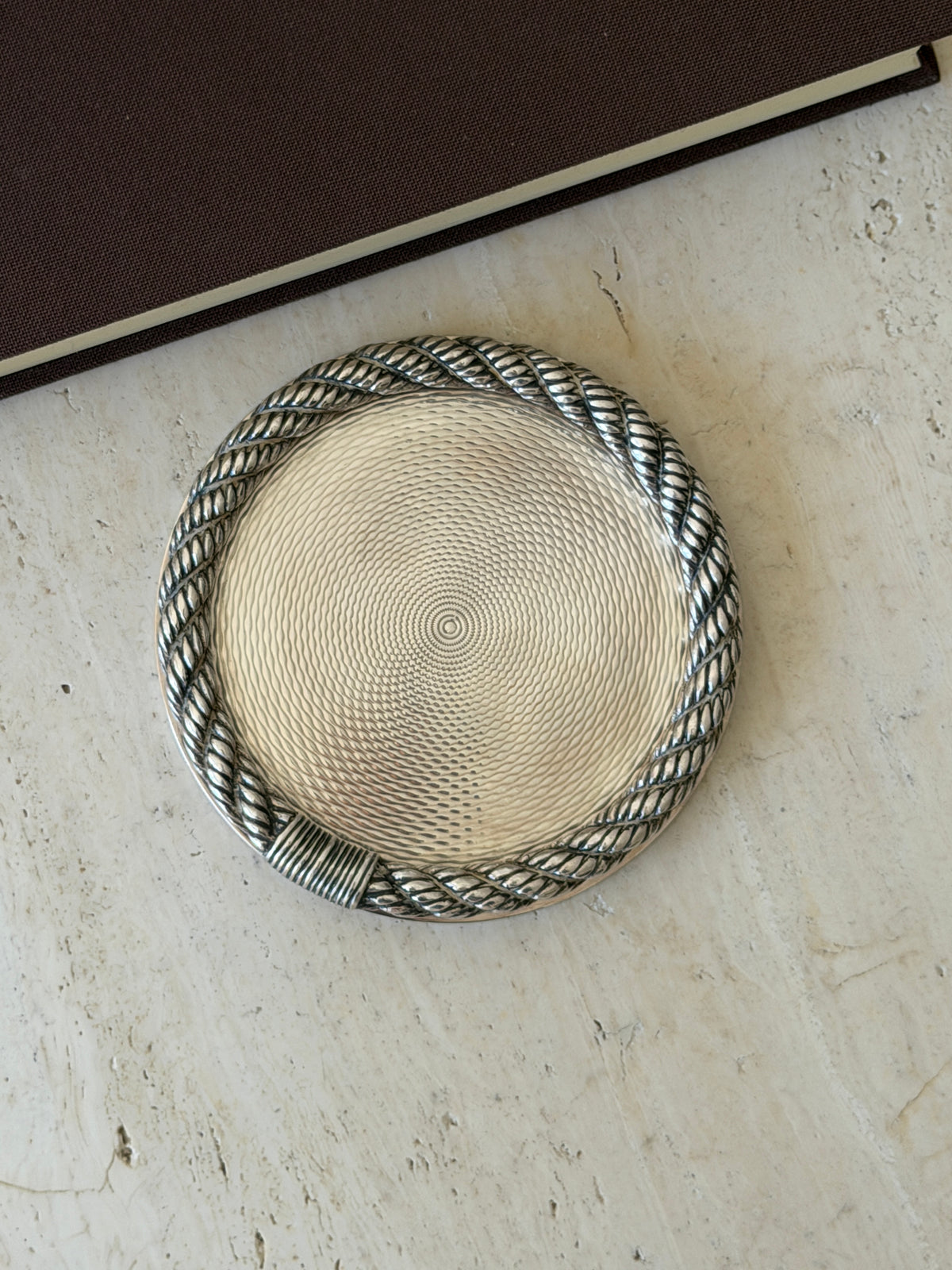 Close overhead view of the Hermes coaster, detailing the fine guilloche pattern and the ribbed rope binding at the base