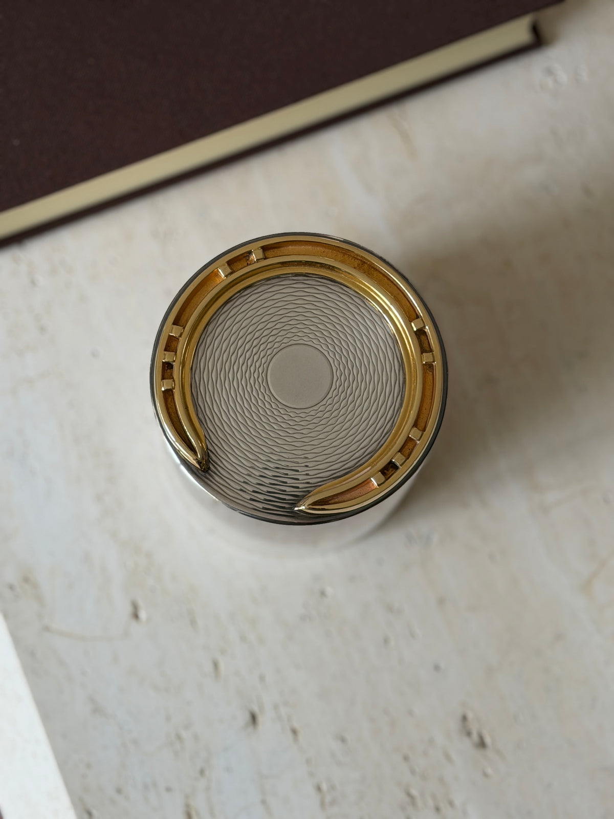 Top-down view of the Hermes cigarette box lid showing the wavy guilloche pattern radiating from a plain center disc inside the gilt horseshoe