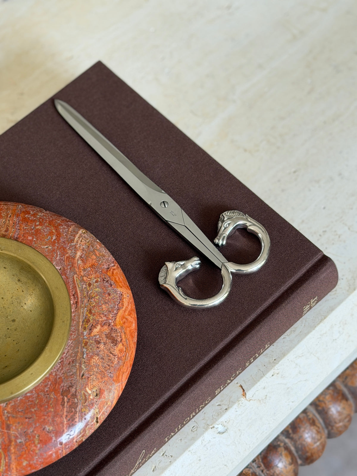 Scissors displayed on a different book, blade pointing away from the stone bowl visible in the background
