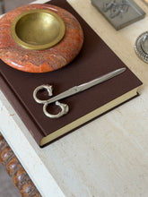 Scissors shown closed on the same book from another angle, with the stone bowl and an engraved metal box nearby