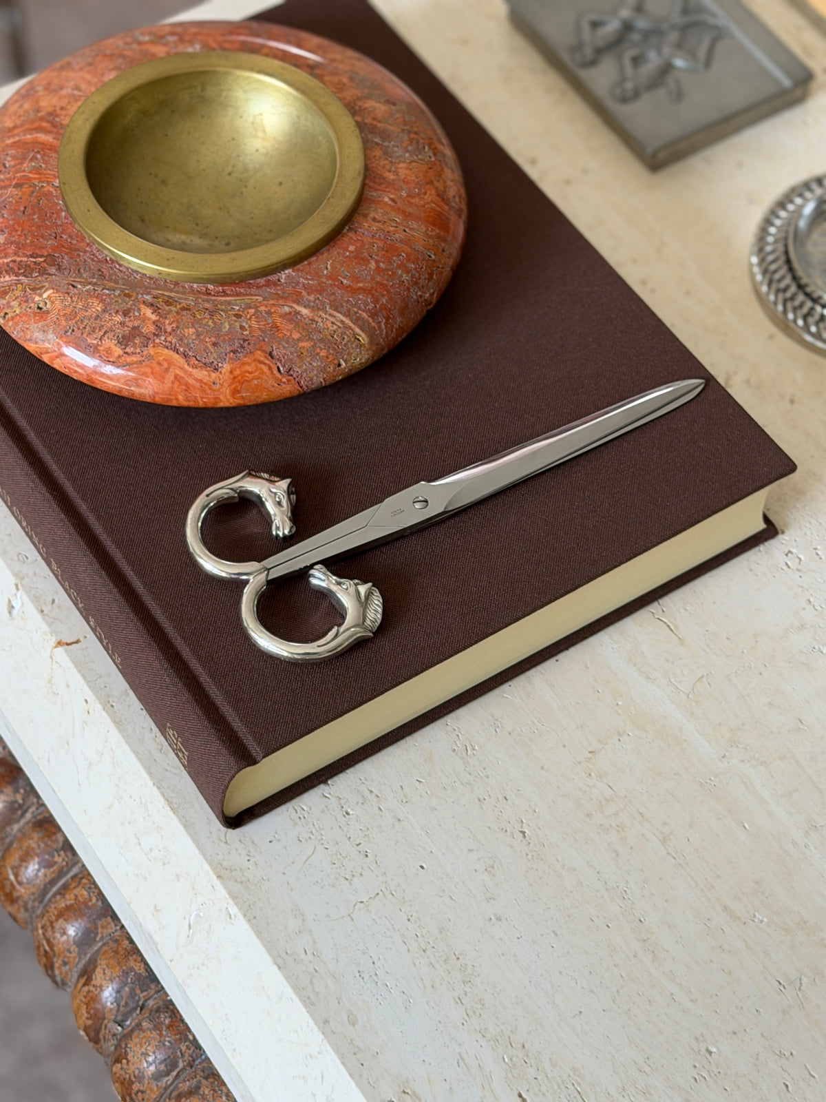 Scissors shown closed on the same book from another angle, with the stone bowl and an engraved metal box nearby
