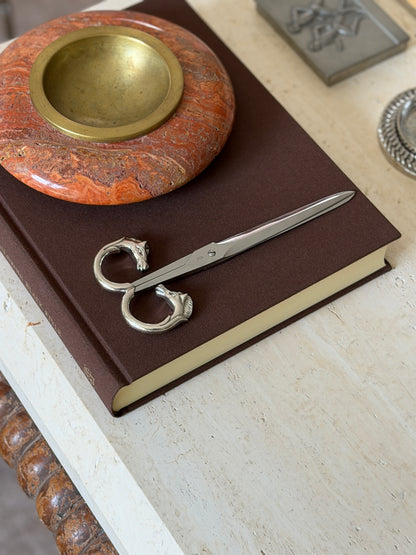 Scissors shown closed on the same book from another angle, with the stone bowl and an engraved metal box nearby