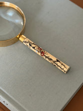 Close view of the Meiji handle on the Hermes magnifying glass, red flower blossoms and mother of pearl leaves inlaid along a dark vine