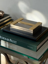 High angle view of closed Hermes silver and brass H logo box on book display available at Collectors Gene
