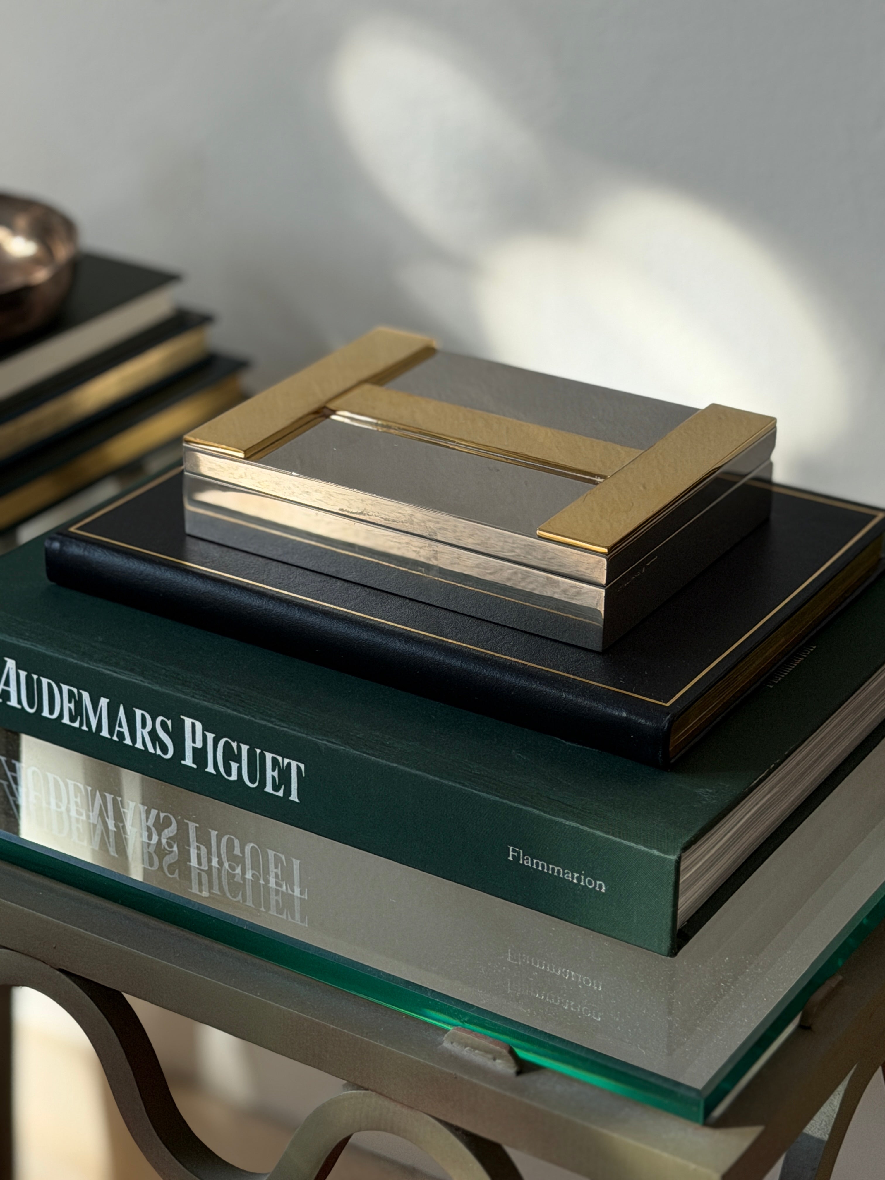 High angle view of closed Hermes silver and brass H logo box on book display available at Collectors Gene