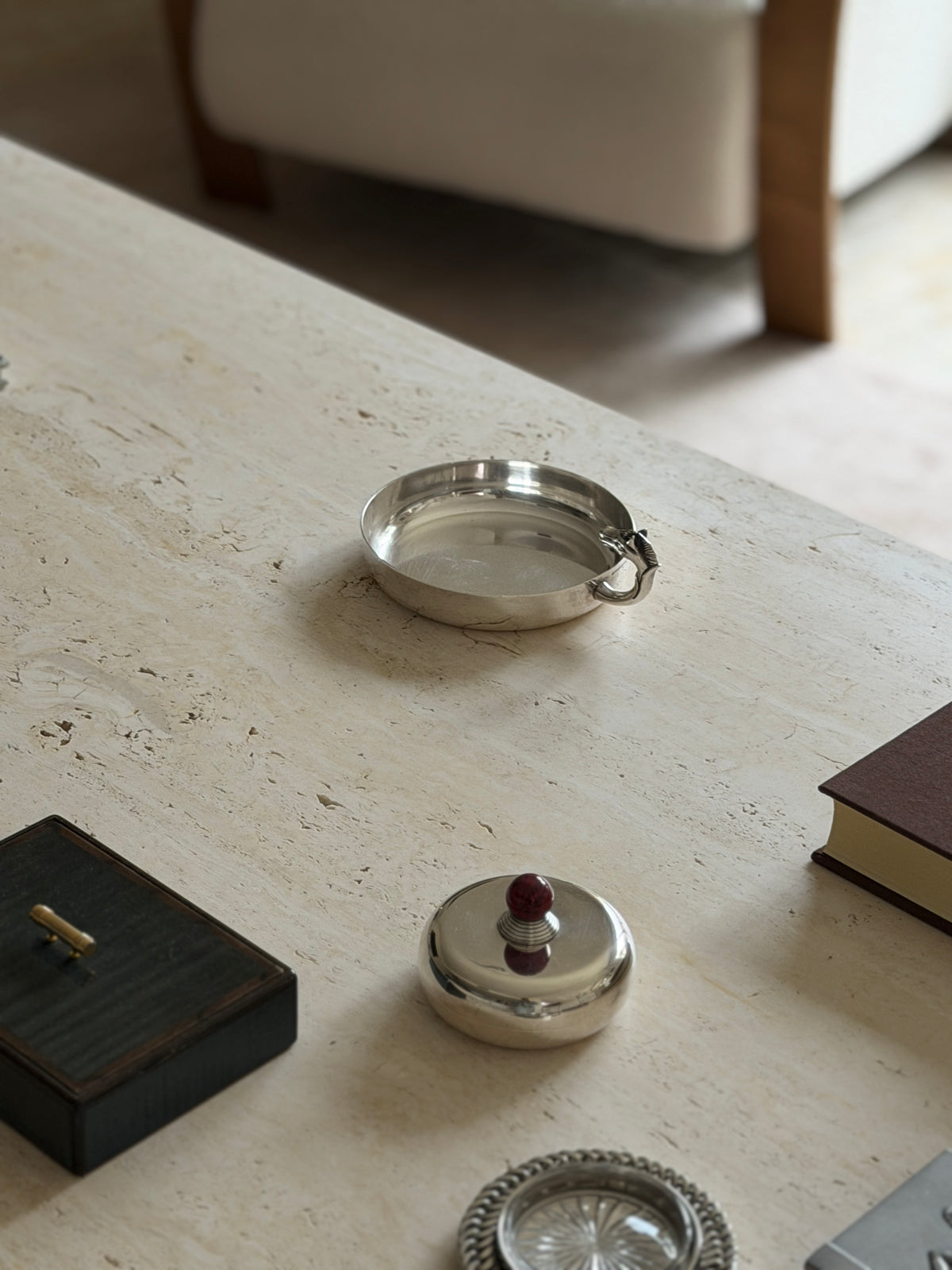 High angle view of the Hermes horse head catchall on pitted travertine, the curved handle rising at the back of the plain silver rim