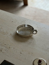 Silver catchall viewed from the opposite side, the horse head handle curling over the rim with a lidded silver box in the foreground