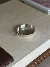 Horse head catchall on a travertine table beside framed artwork, small stamped marks visible on the outer rim near the handle