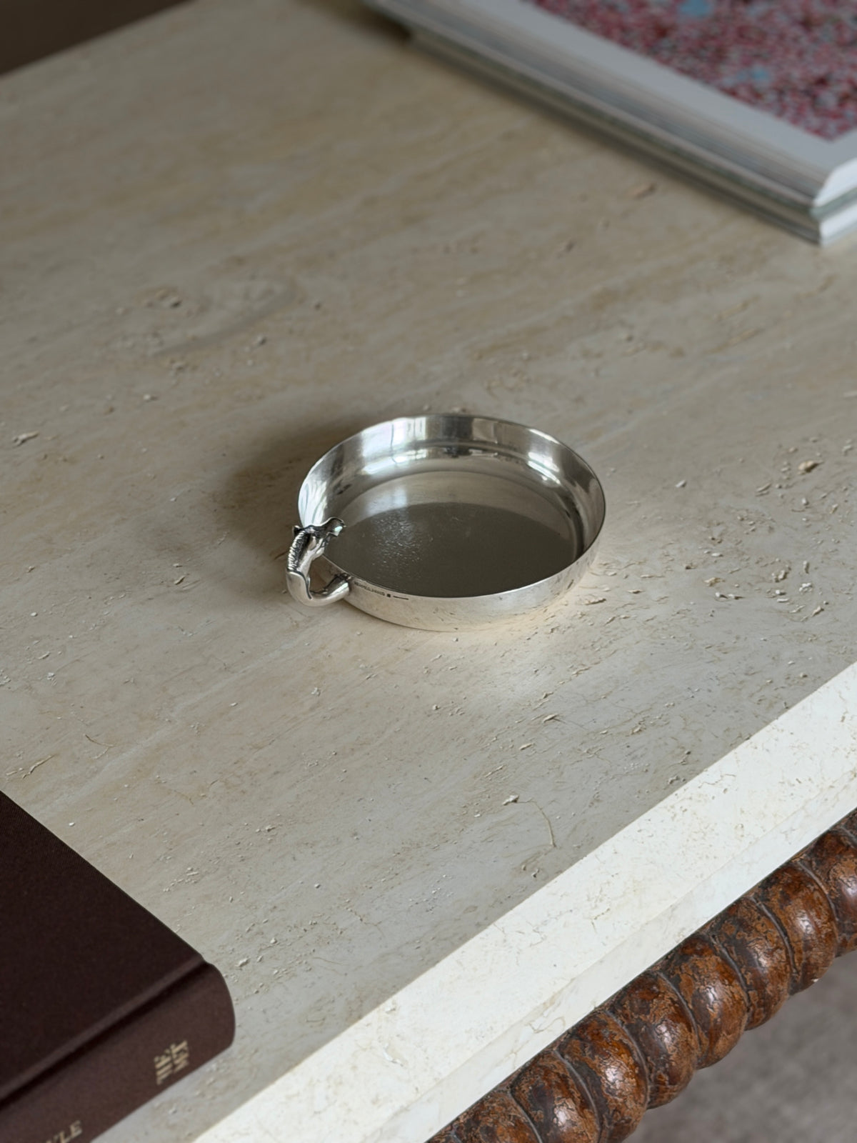 Horse head catchall on a travertine table beside framed artwork, small stamped marks visible on the outer rim near the handle