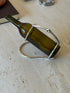 Hermes horse bit wine caddy holding an olive green bottle at a pouring angle on a travertine table