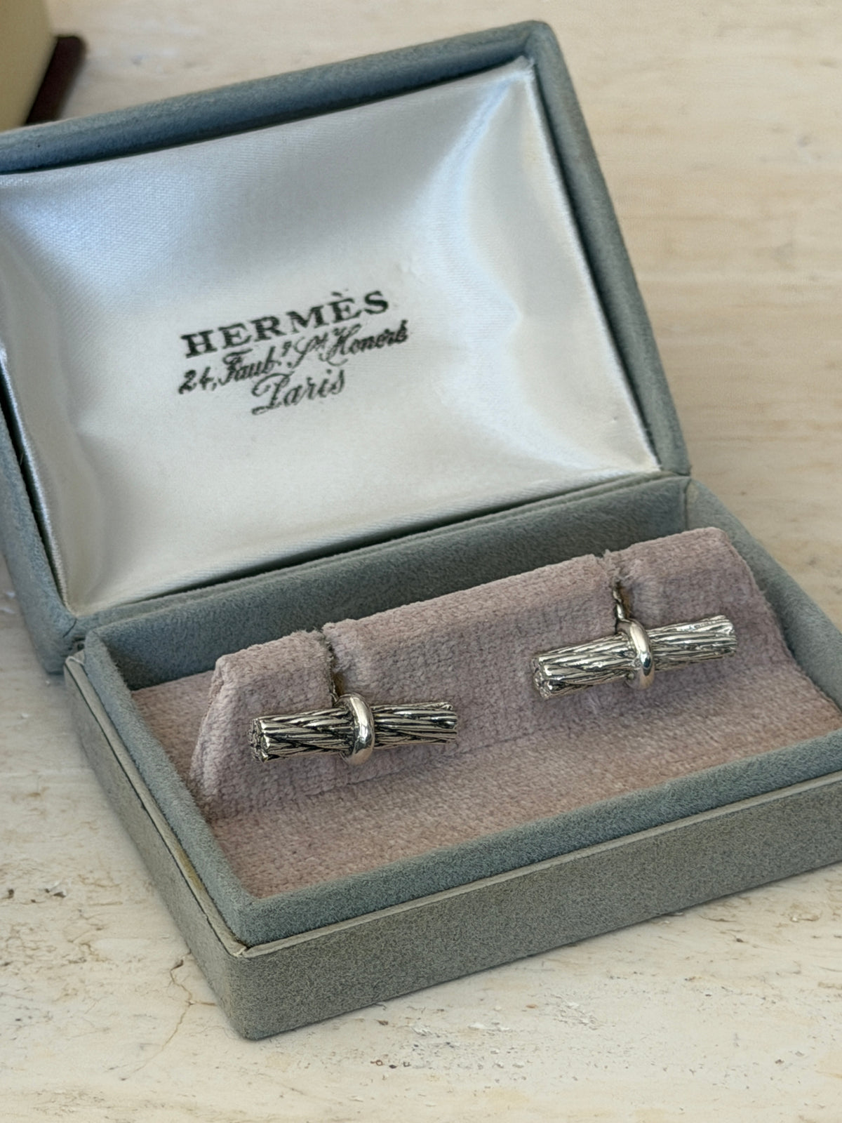 Pair of Hermes rope bar cufflinks set on the lilac velvet cushion of their original gray suede presentation box