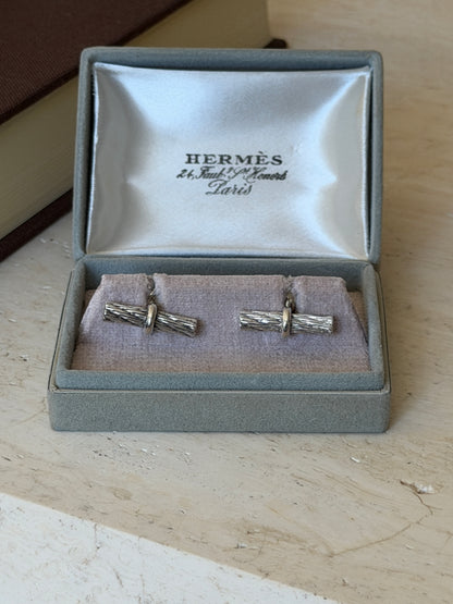 Front view of the open Hermes box with both rope bar cufflinks seated on the cushion below the satin lid lining