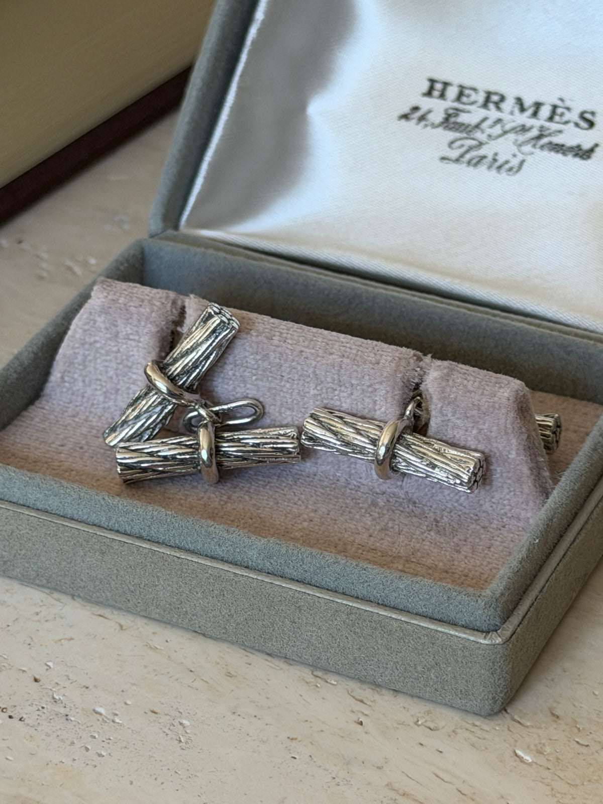 Hermes rope cufflinks shown loose in the box, revealing the chain link connecting each twisted bar to its matching back