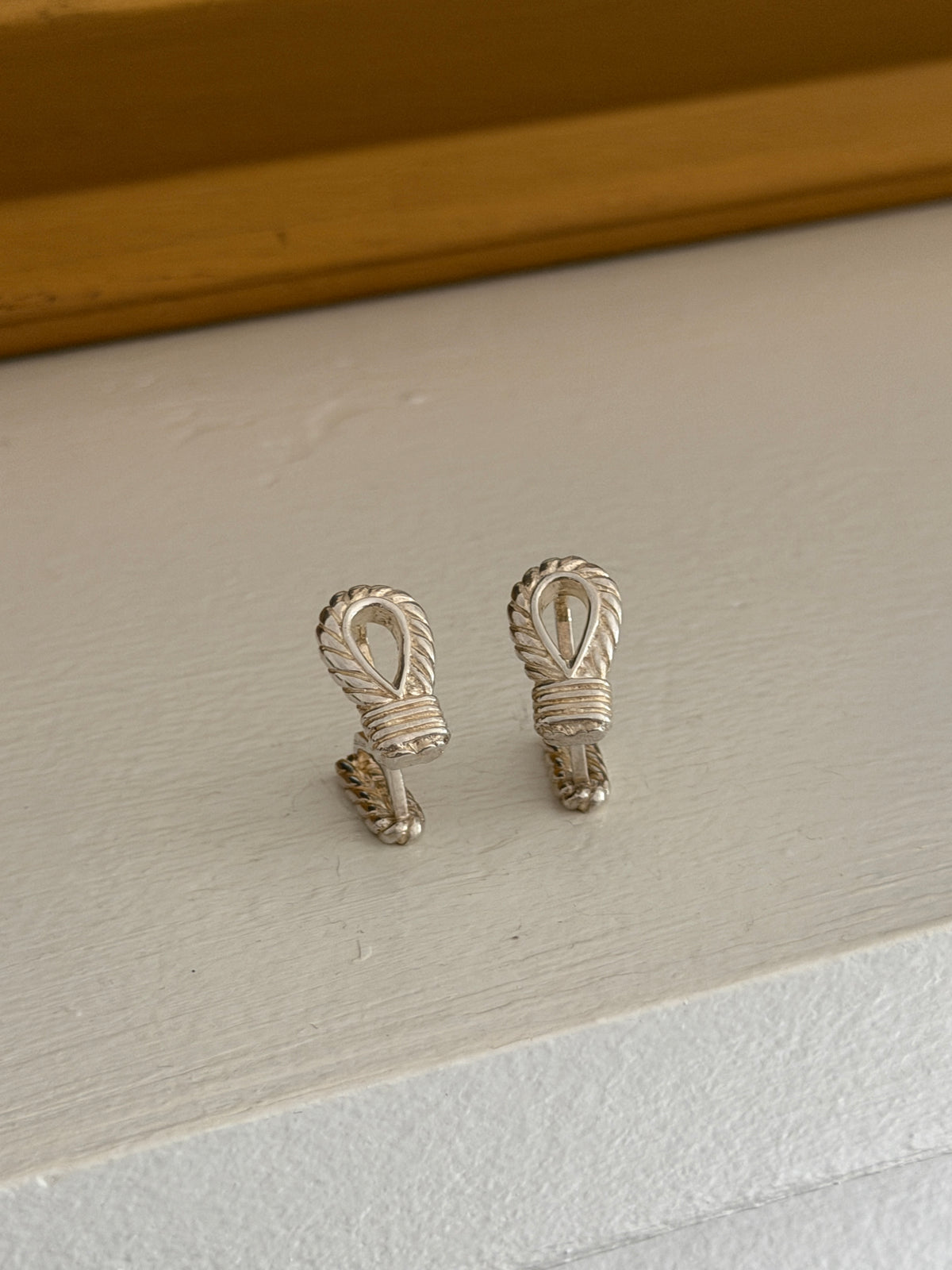 Hermes rope motif cufflinks side by side, each a teardrop loop of twisted rope bound by a ribbed silver wrapping