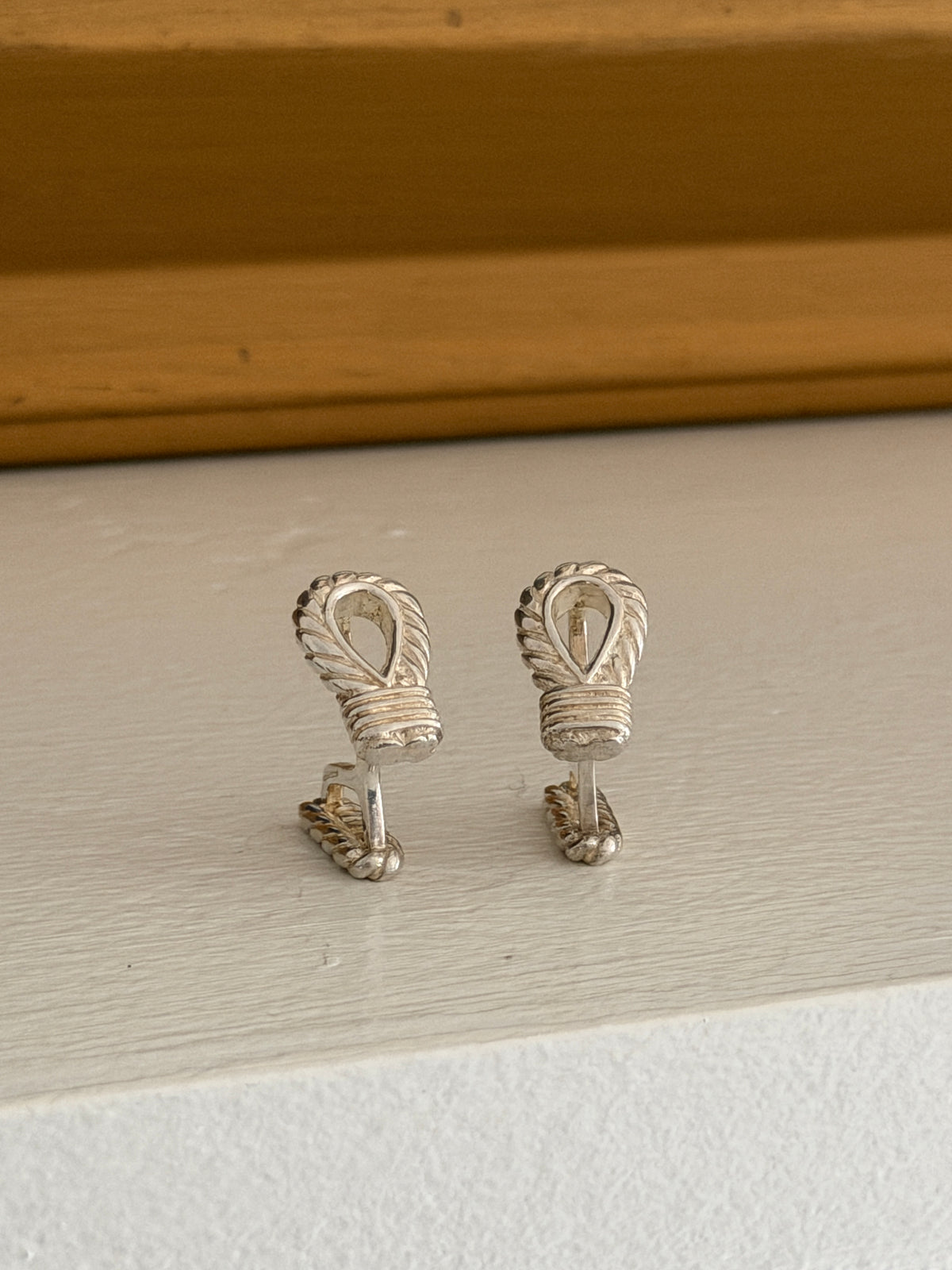 Front view of the Hermes rope loop cufflinks on a white ledge against a warm wood molding