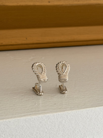 Front view of the Hermes rope loop cufflinks on a white ledge against a warm wood molding