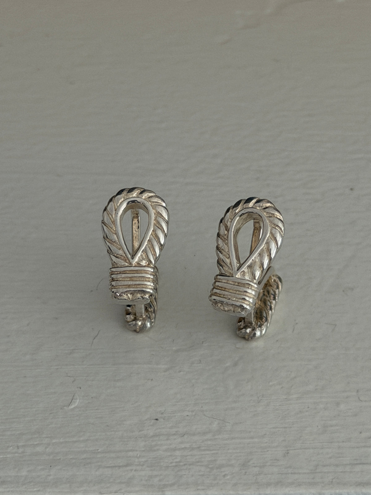 Overhead view of the silver rope cufflinks, detailing the carved rope twist around each open loop and the banded knot