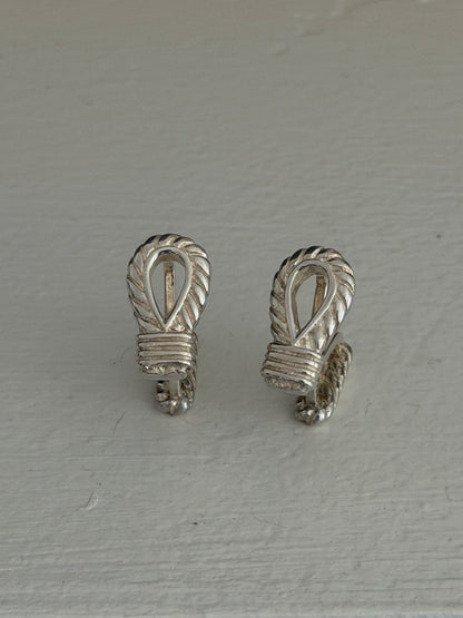 Overhead view of the silver rope cufflinks, detailing the carved rope twist around each open loop and the banded knot