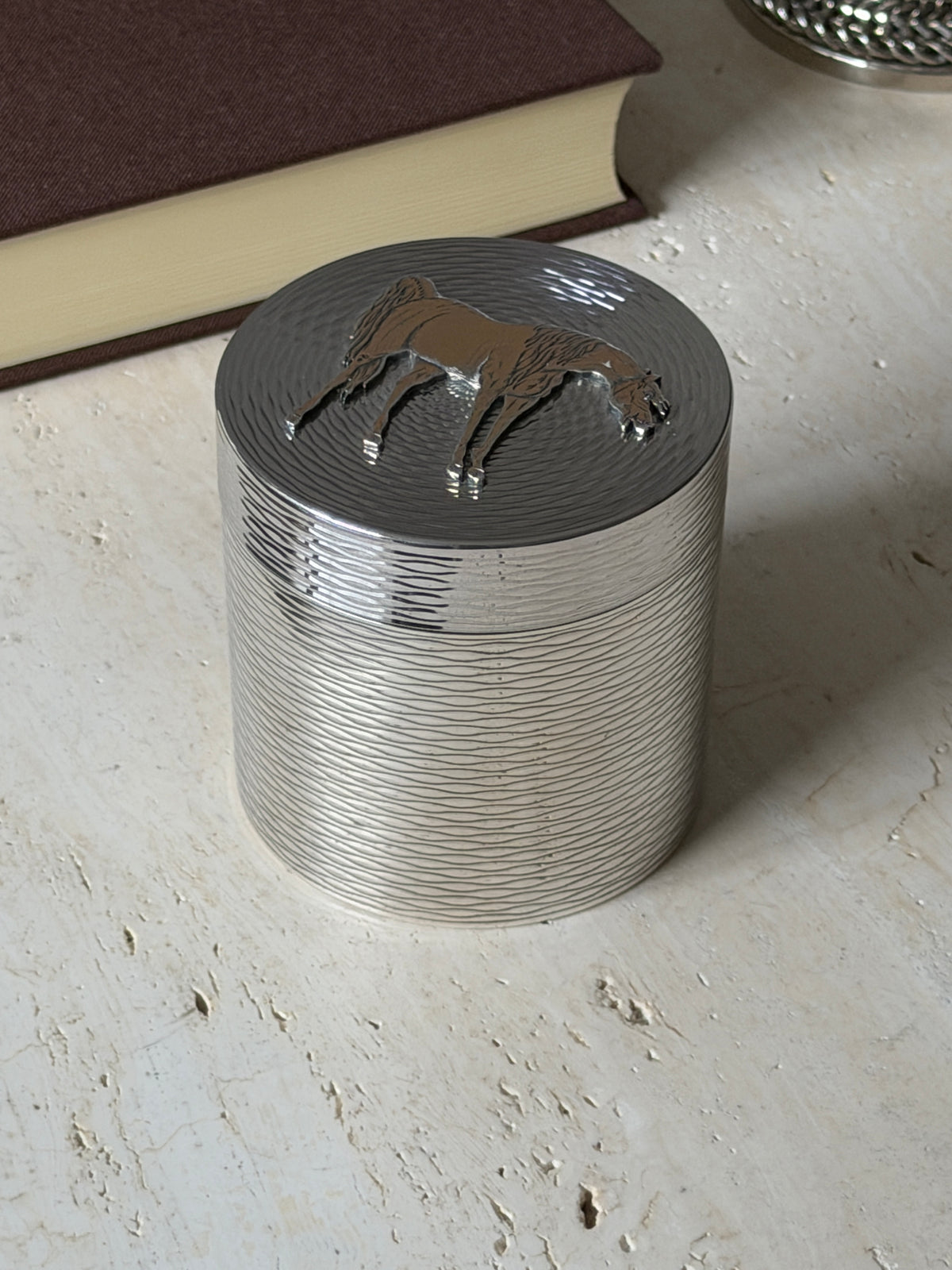 Angled close view of the Hermes box, the gilt horse in raised relief above the textured lid and wavy engraved sides