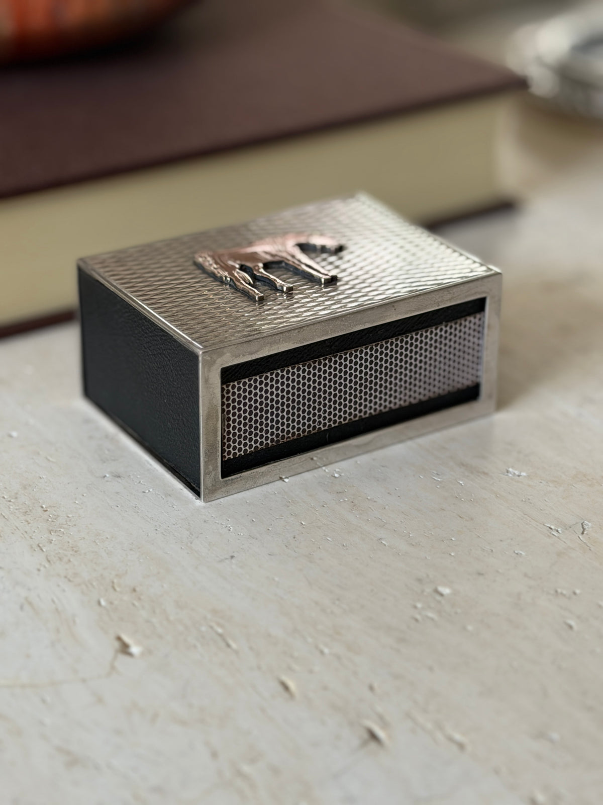 Low side view of the Hermes matchbox showing the black leather sides and the striker panel framed in silver below the gilt horse