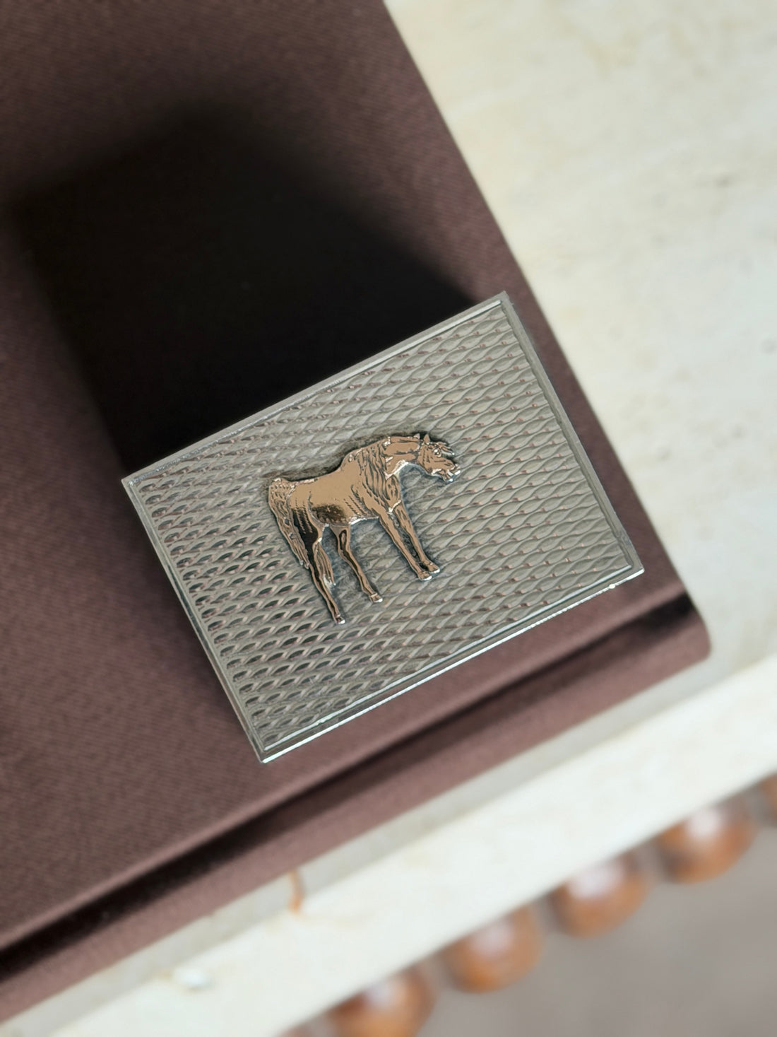 Close overhead view of the Hermes matchbox lid, the gilt horse in relief against diagonal engine turned silver