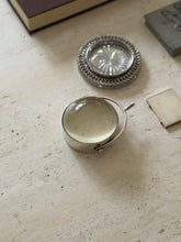 The magnifier shown alongside a woven silver-rimmed coin tray and the corner of a picture frame on a stone surface