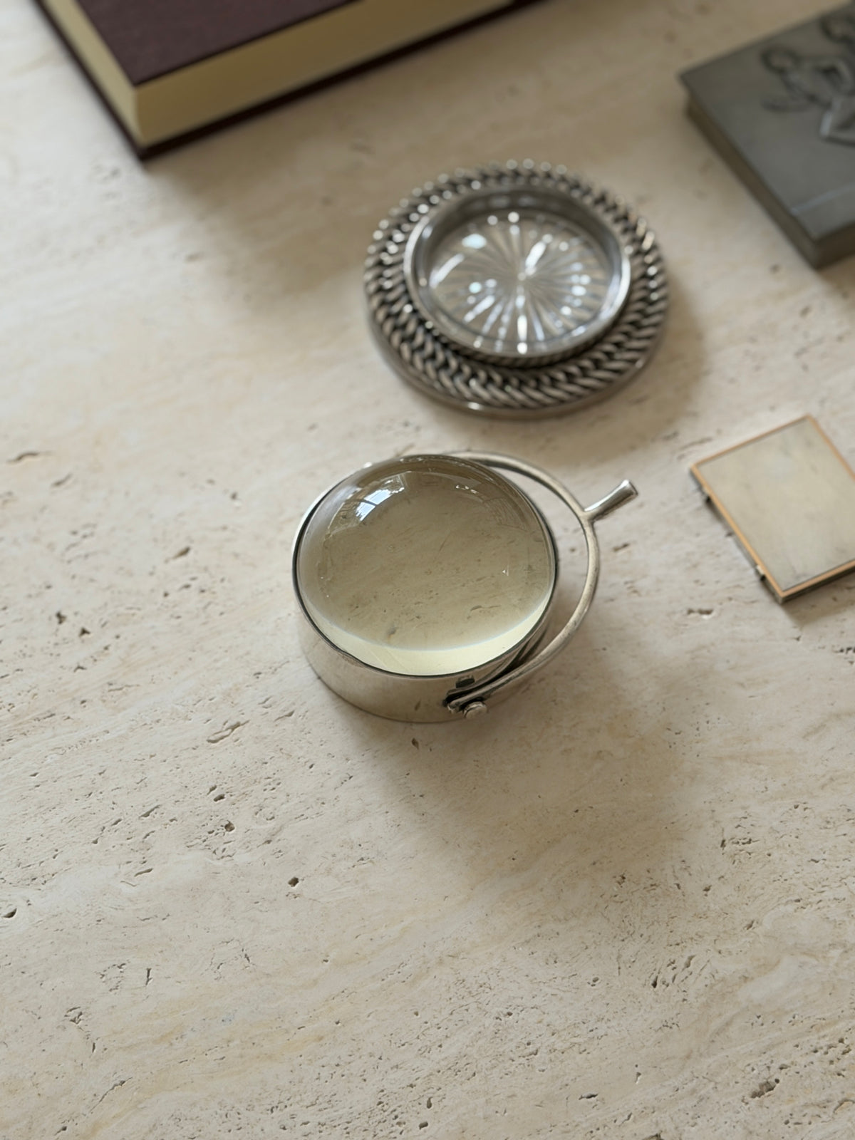The magnifier shown alongside a woven silver-rimmed coin tray and the corner of a picture frame on a stone surface