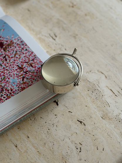 Close-up of the magnifier resting on the edge of an open book with a pink floral illustration, showing the spur handle in detail