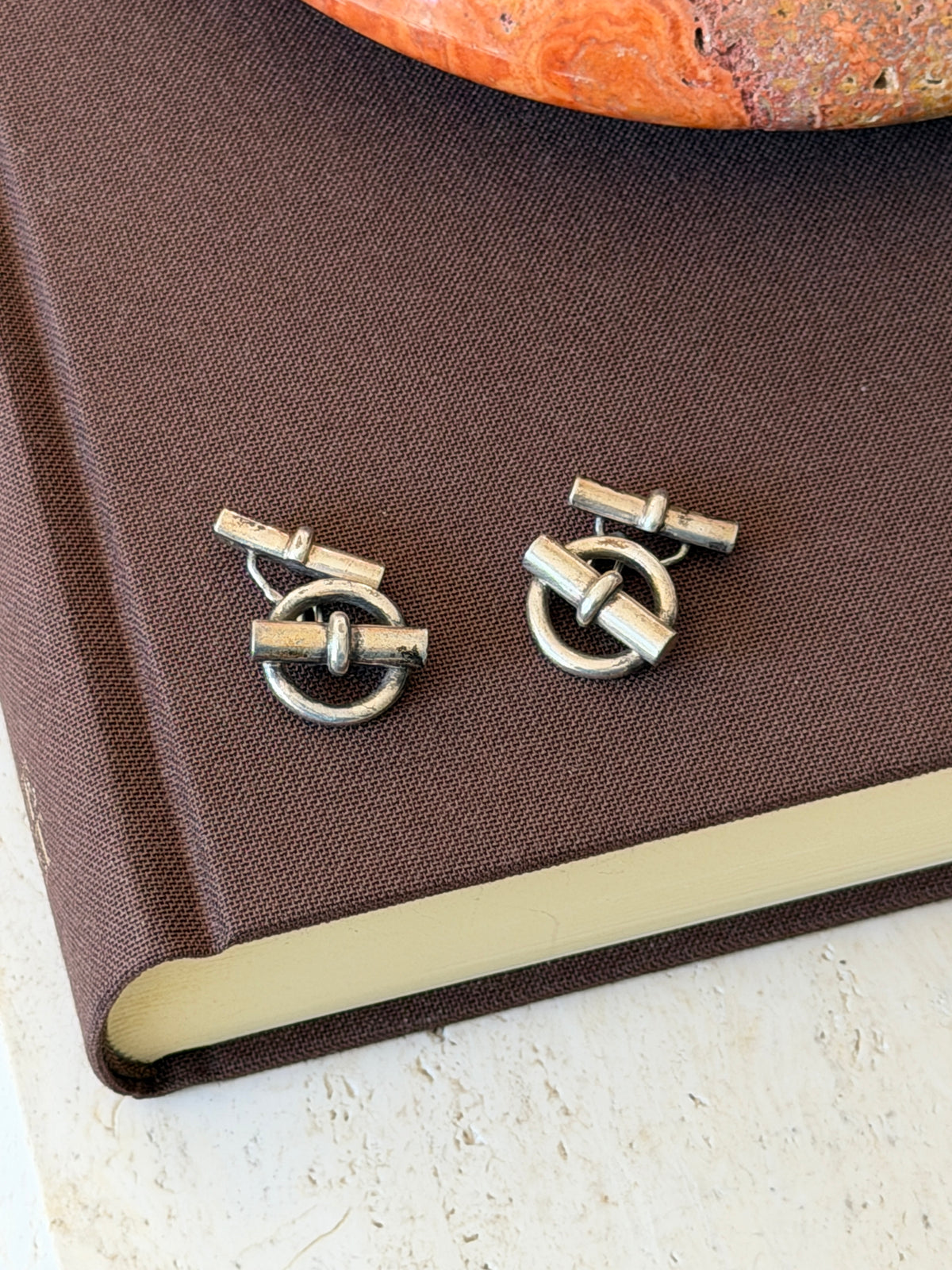 Silver ring and bar cufflinks on a brown linen book cover, showing the chain joining each front ring to its toggle back