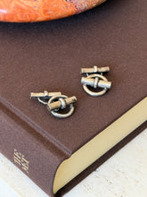 Angled view of the ring and toggle cufflinks on the corner of a brown book, patina visible on the rounded bars
