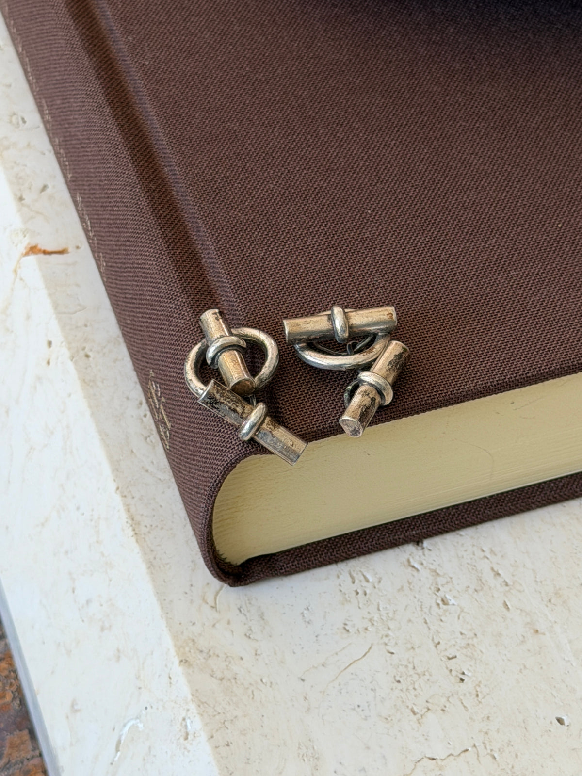 Silver toggle cufflinks tumbled on the edge of a brown book, showing the ring fronts, short chains, and bar backs