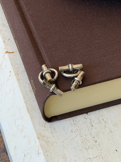 Silver toggle cufflinks tumbled on the edge of a brown book, showing the ring fronts, short chains, and bar backs