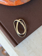 Hermes sterling silver money clip formed as an oval loop wrapped by a belt strap with buckle, keeper, and pierced holes, on a brown book