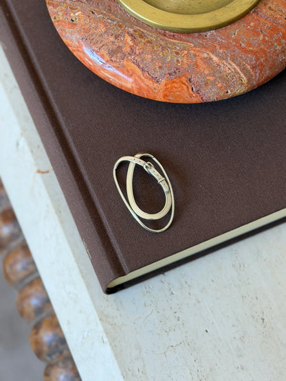 Belt buckle motif money clip on the corner of a brown book beneath a red stone ashtray, a bobbin turned table leg below
