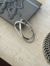 Belt strap money clip leaning against a pewter relief box on travertine, showing the sprung double loop