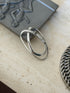 Belt strap money clip leaning against a pewter relief box on travertine, showing the sprung double loop