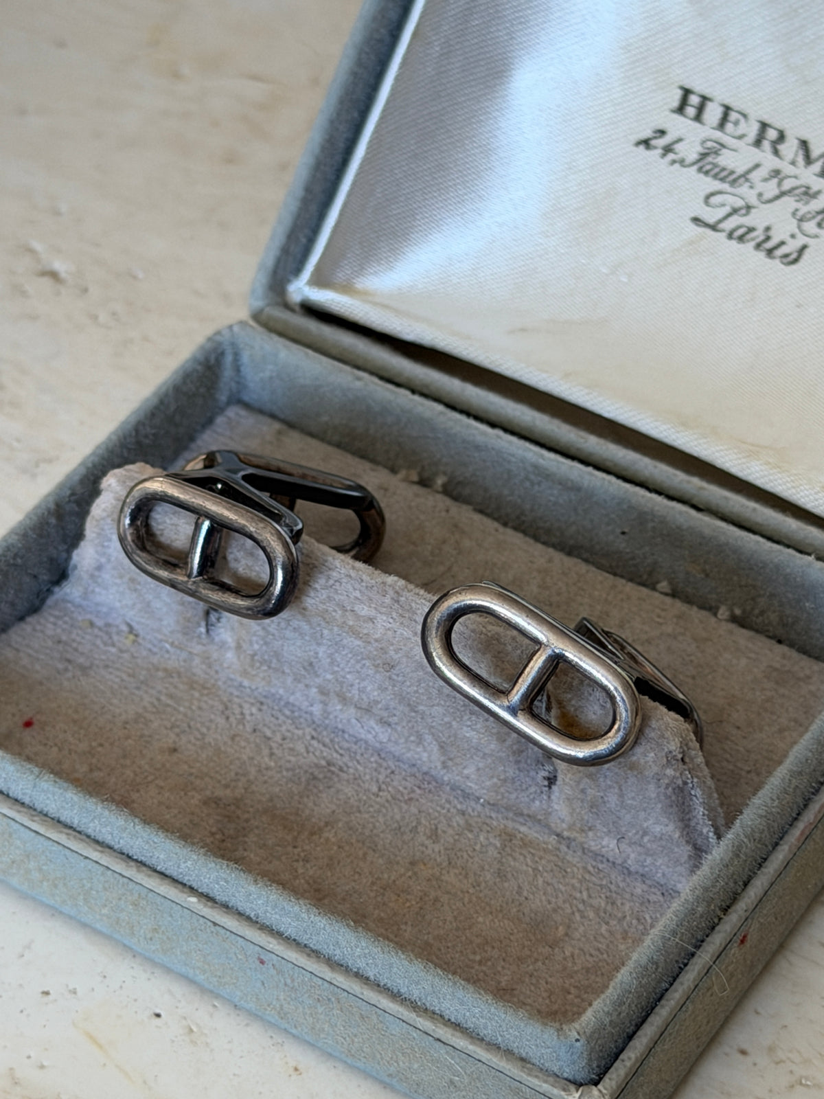 Close view of the Hermes anchor chain cufflinks on the worn suede cushion, one turned to reveal its hinged back