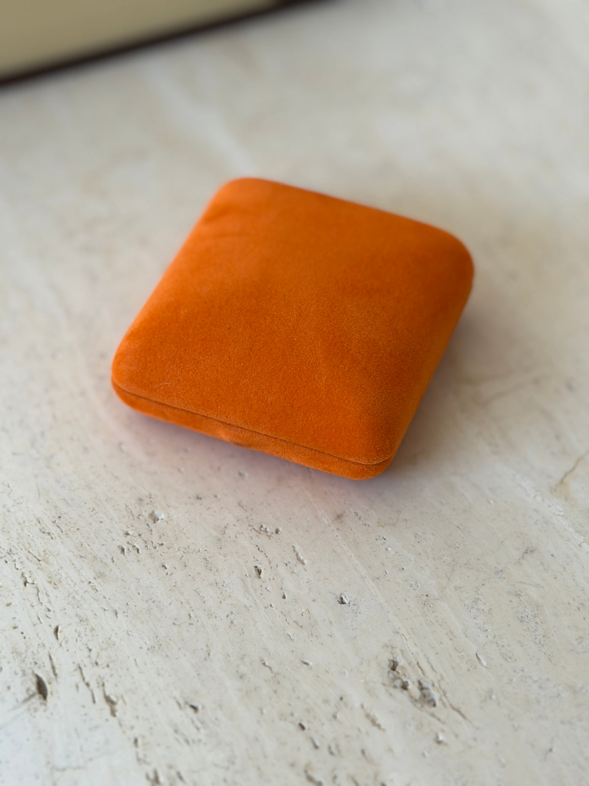 Closed orange suede Hermes presentation box with rounded corners on a travertine surface