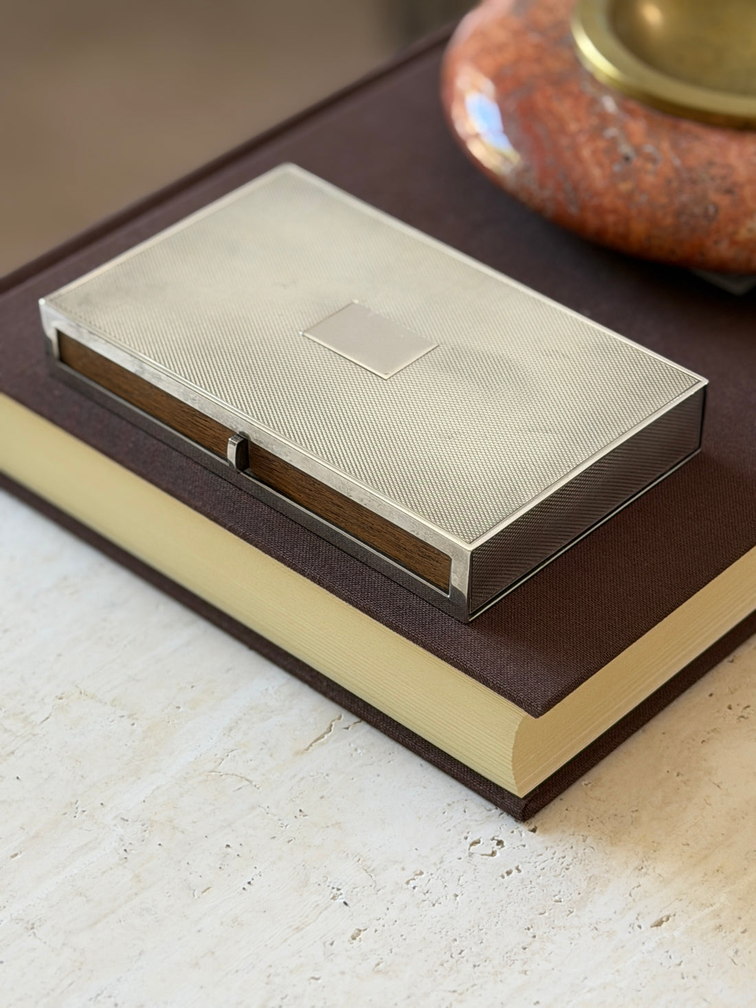 Side angle view of the closed Hermes engine turned silver box on a marble surface