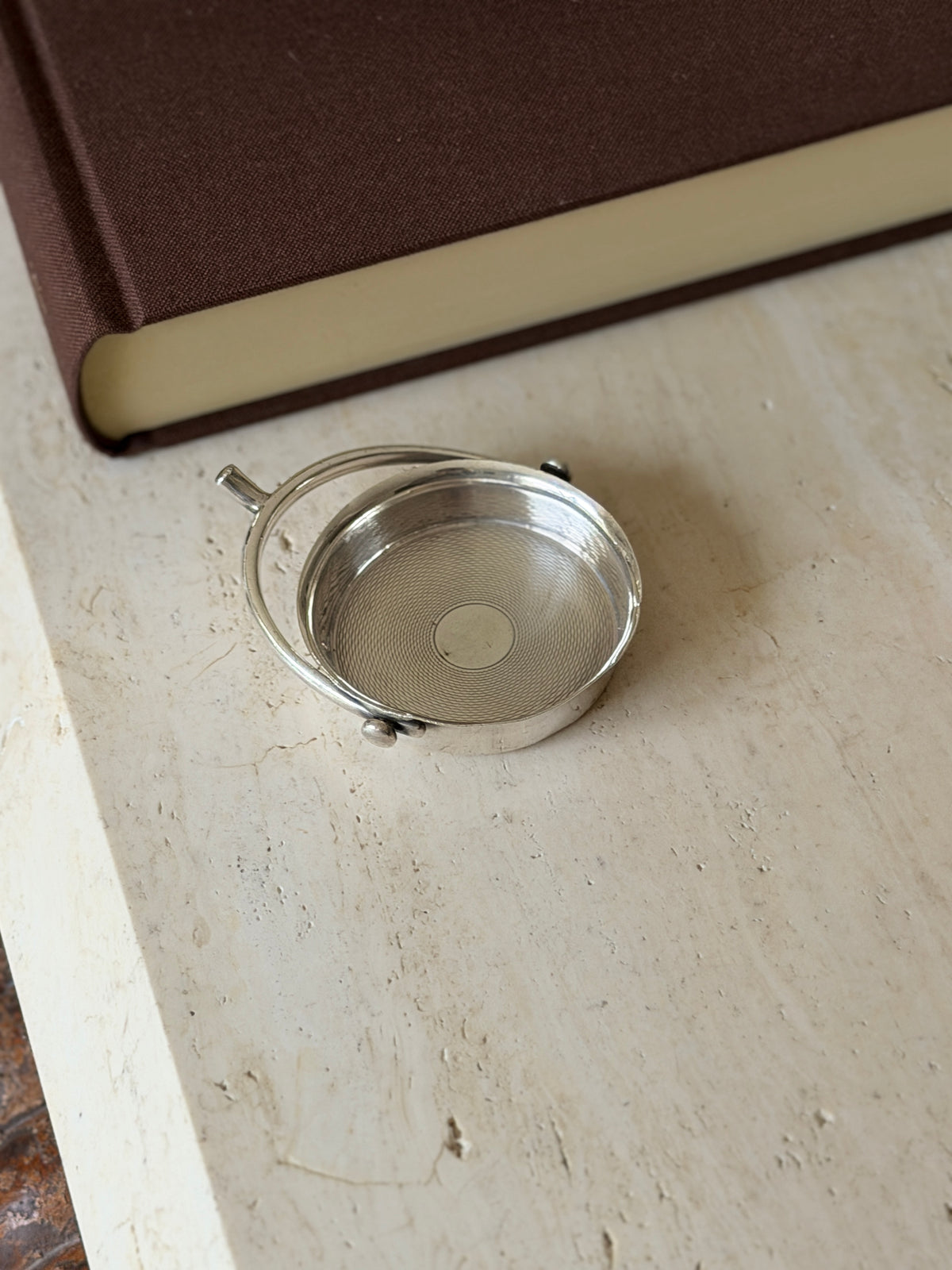 Angled view of the spur catchall, the projecting stem and curved hoop framing the guilloche interior and polished rim