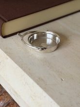Low angle view of the Hermes spur ashtray on travertine, light catching the engine turned pattern and the ball end pivot