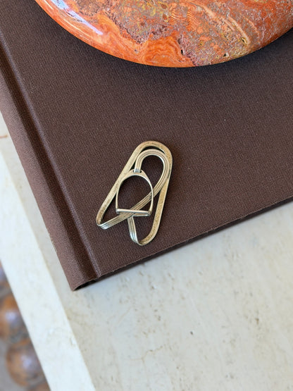 Hermes stirrup money clip on a brown book, a miniature stirrup threaded on an engraved strap inside an oval silver loop